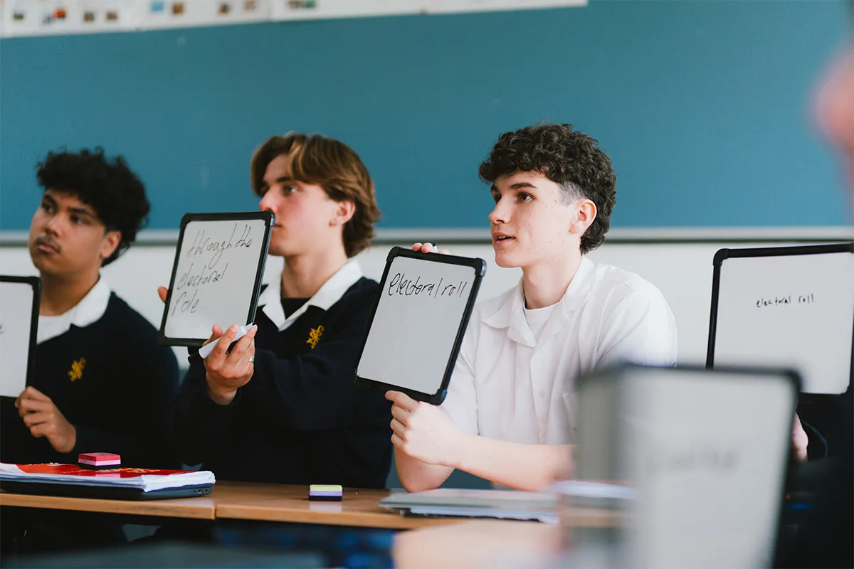 Students in a class holding up tablets with writing on them